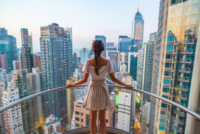 白天，站在灰色不锈钢栏杆旁的女人在高楼大厦中观赏城市